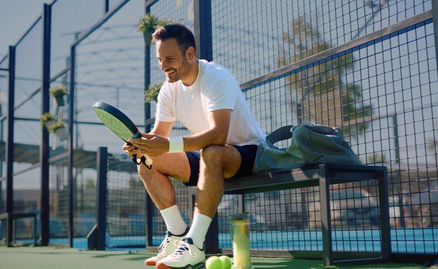 male padel player looking at padel racket on the court