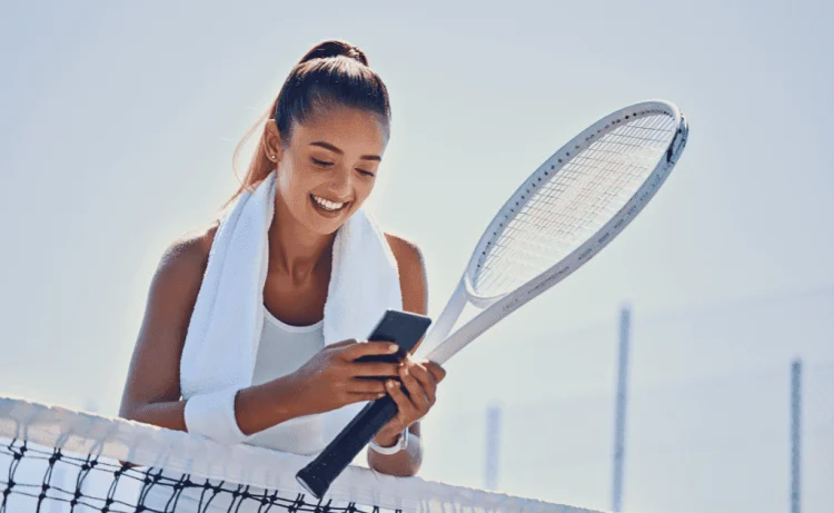 active, fit, and happy female tennis player on the tennis court browsing her smartphone
