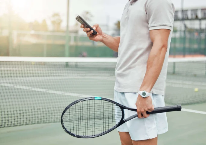 tennis player on his phone on a tennis court with a racket in hand, looking for the next tennis & padel racket