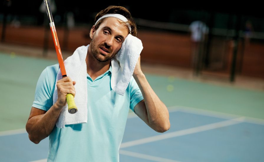 tired and frustrated male tennis player on a tennis court holding a racket and a towel