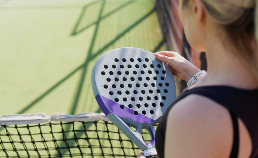 a woman padel player holding a used padel racket in hand and looking at it