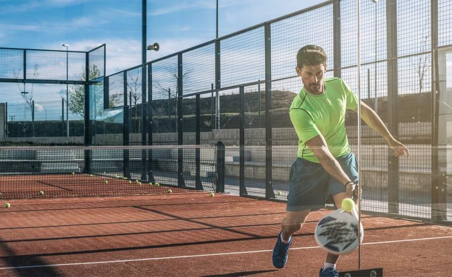 man playing padel hitting the back glass with ball